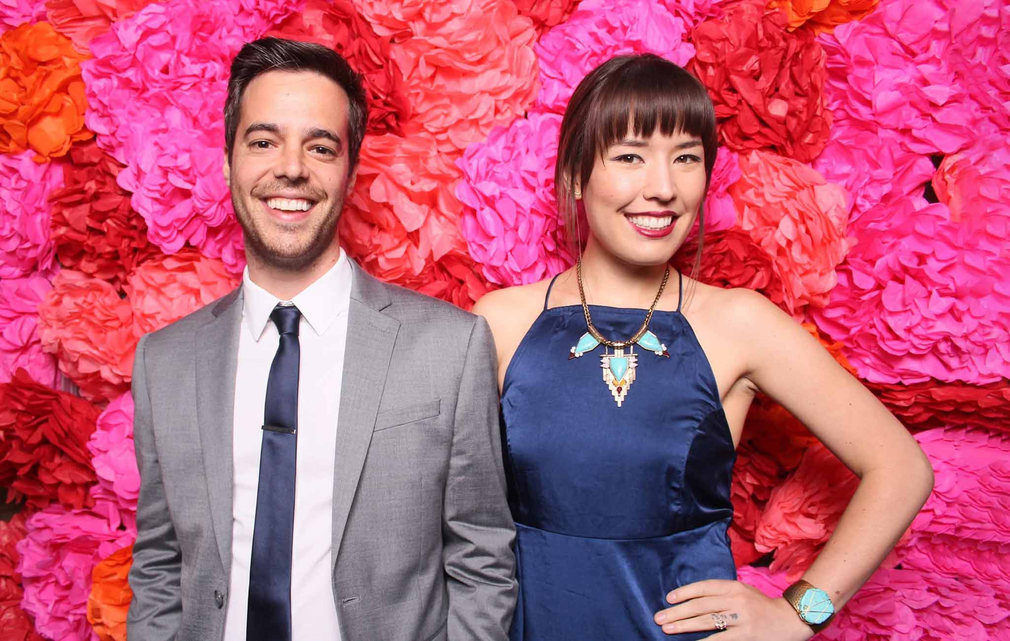 Couple smiling in front of a pink paper flower wall
