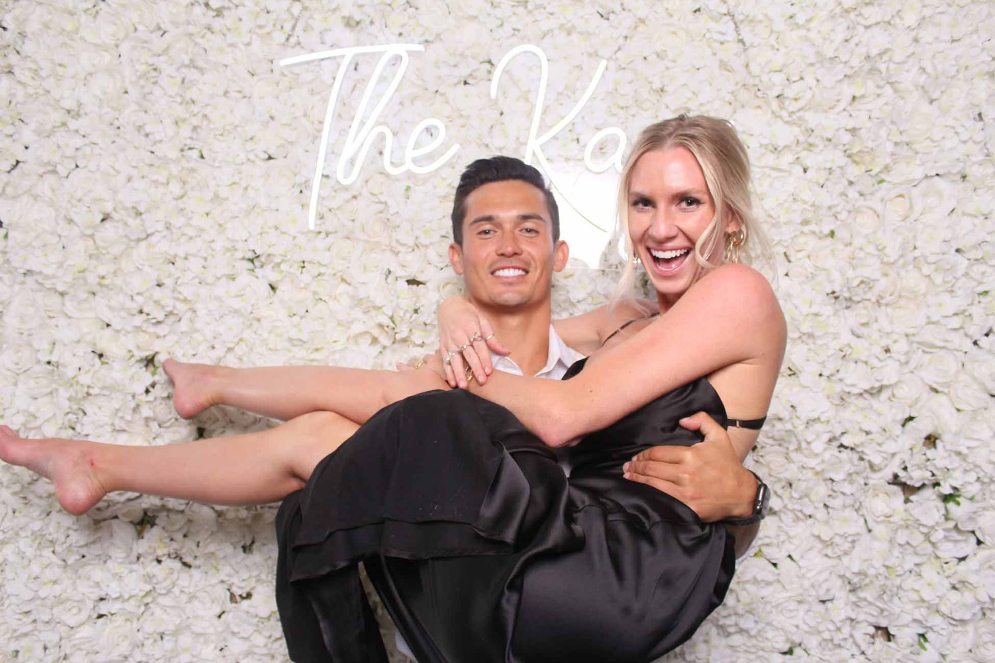 Groom lifting the bride in front of a flower wall