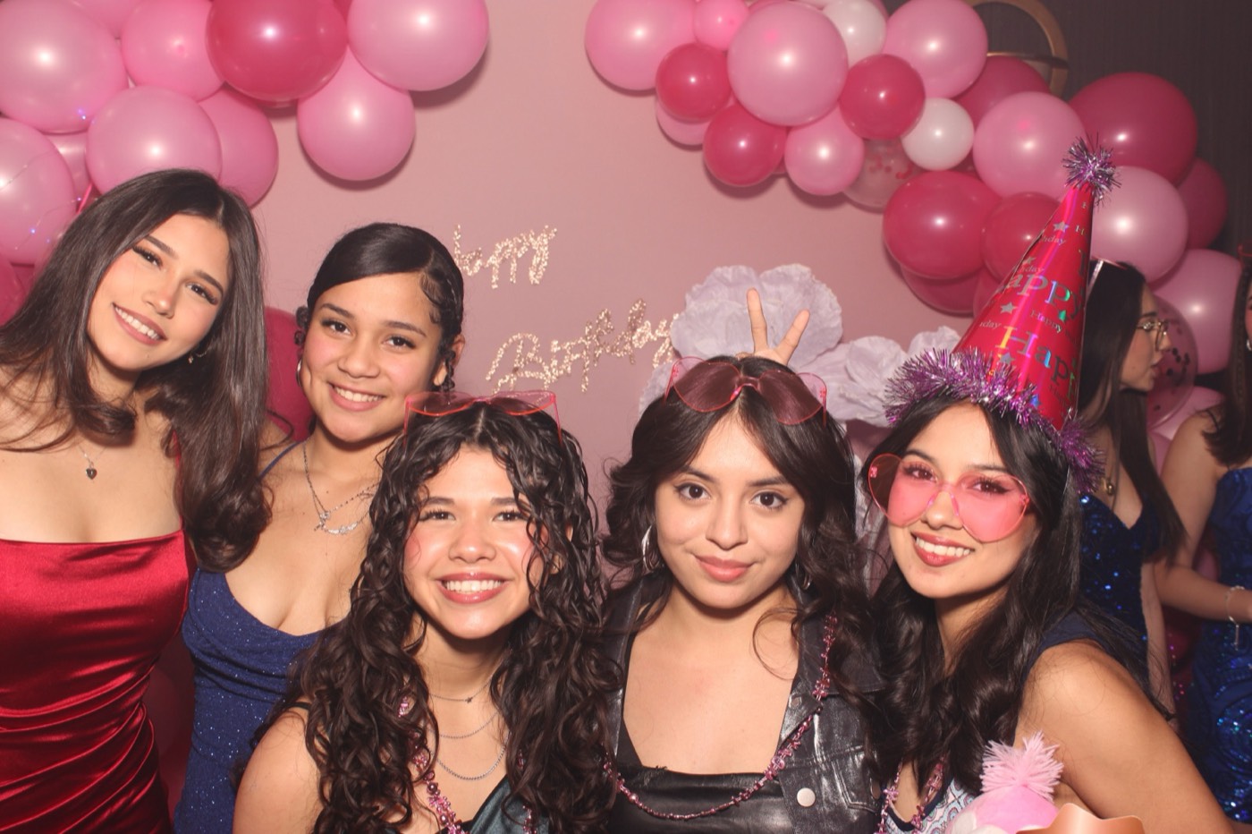 Friends in party dresses in front of a pink balloon arch at a birthday party