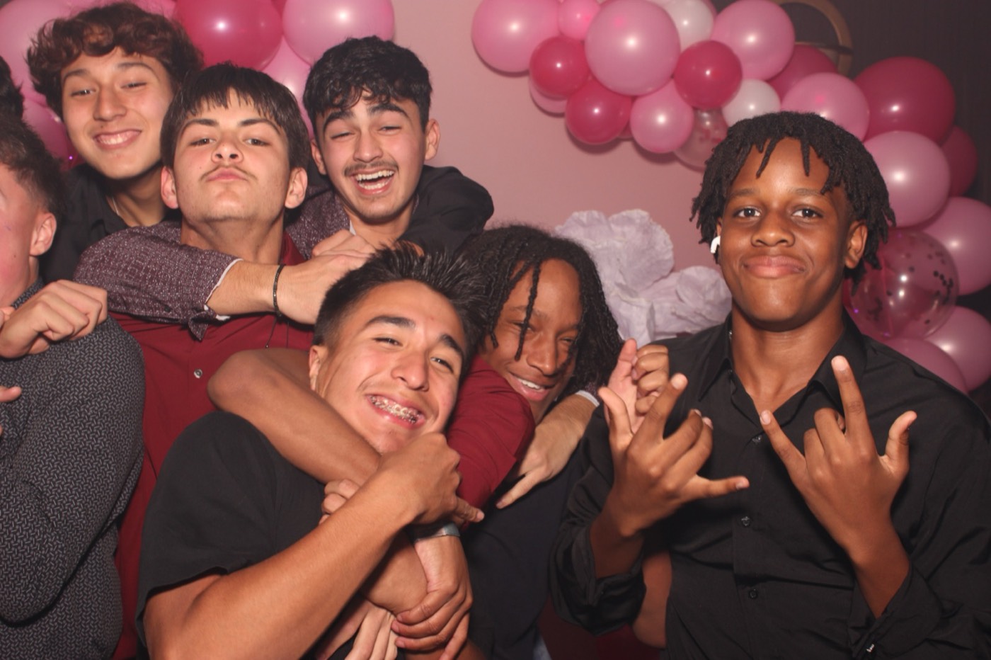 A group of boys throwing hand signs in front of a pink balloon arch at a birthday party