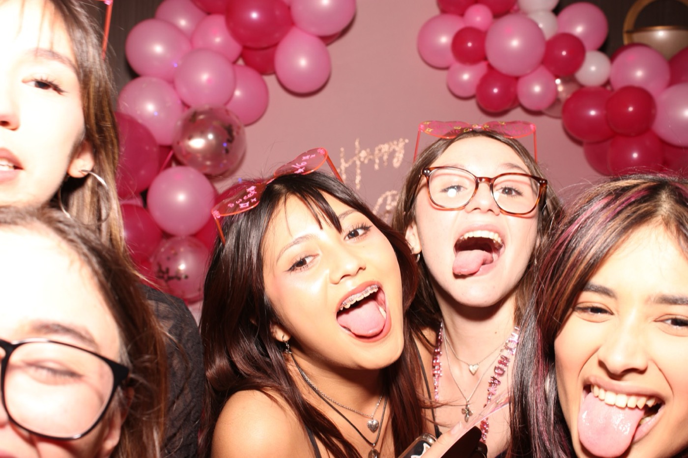 Friends laughing up close in front of a pink balloon arch at a birthday party