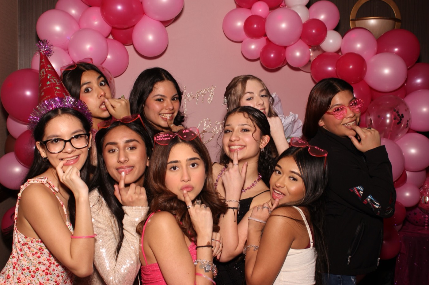 A big group of girls in front of a pink balloon arch at a birthday party