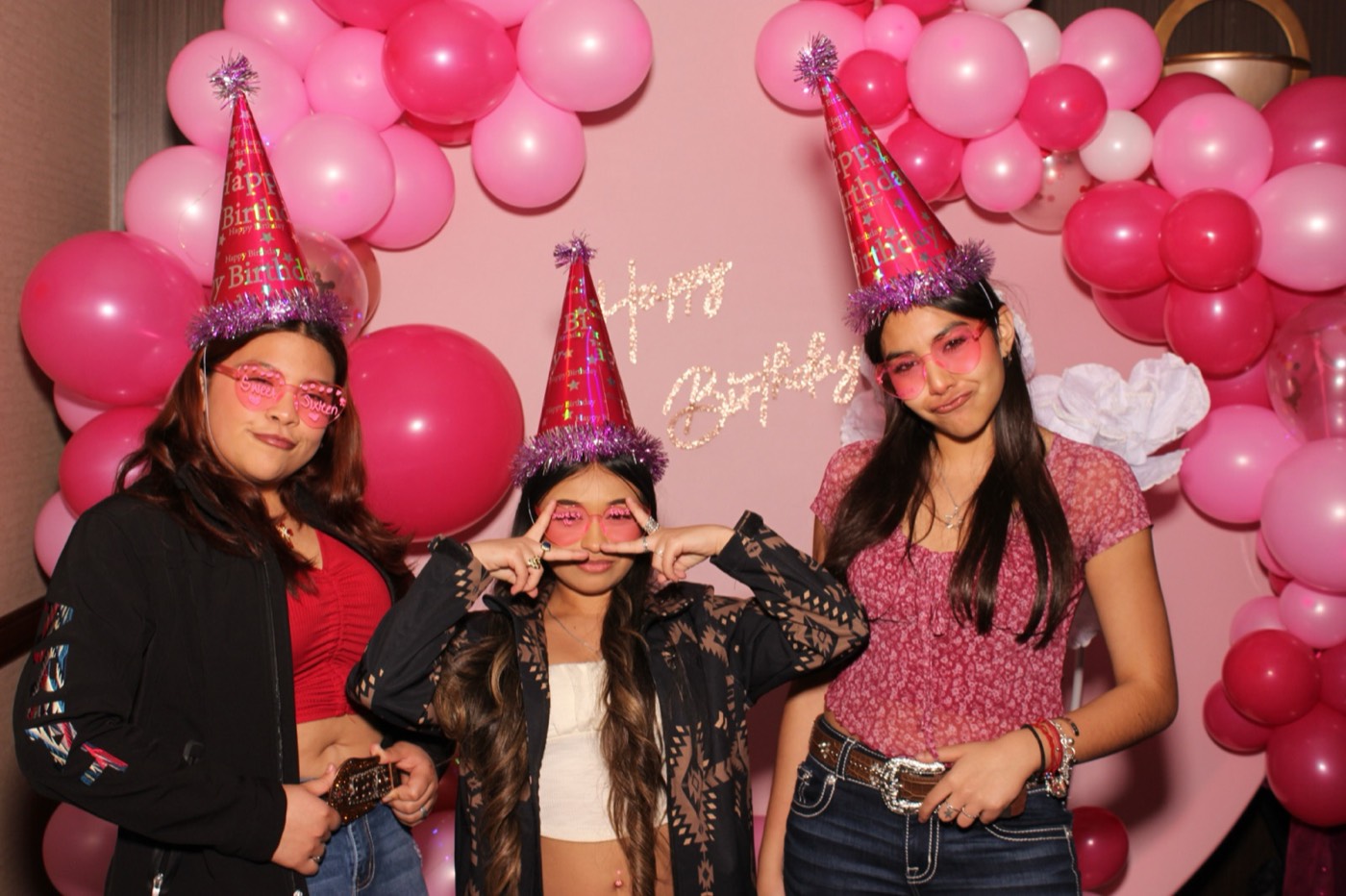 Friends in party hats in front of a pink balloon arch at a birthday party