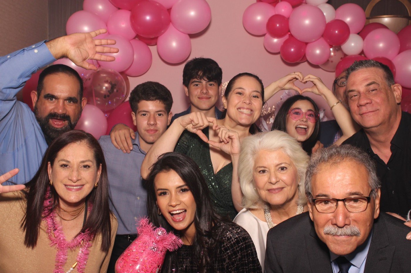 Three generations of family in front of a pink balloon arch at a birthday party