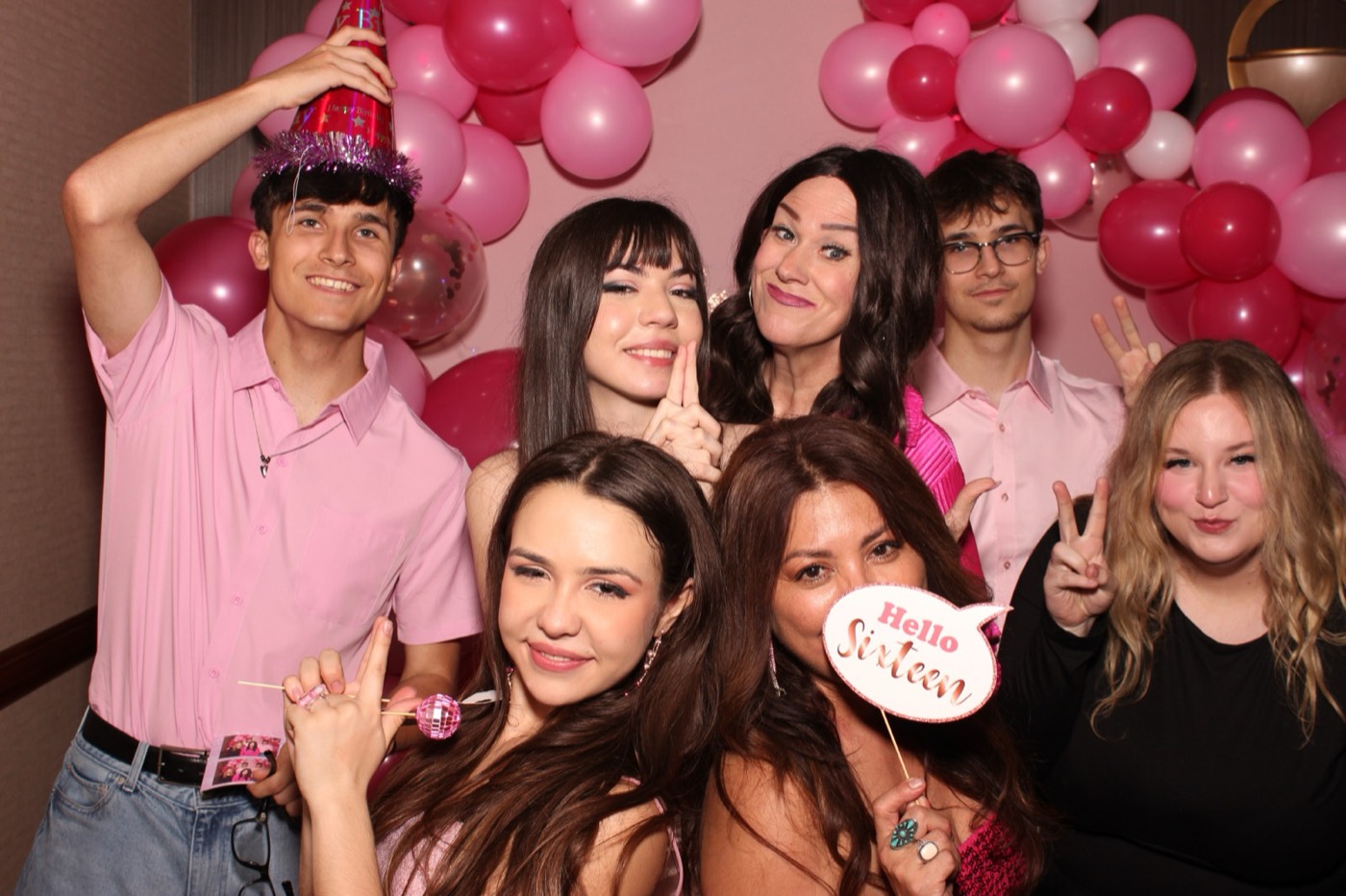 A group holding a party sign in front of a pink balloon arch at a birthday party