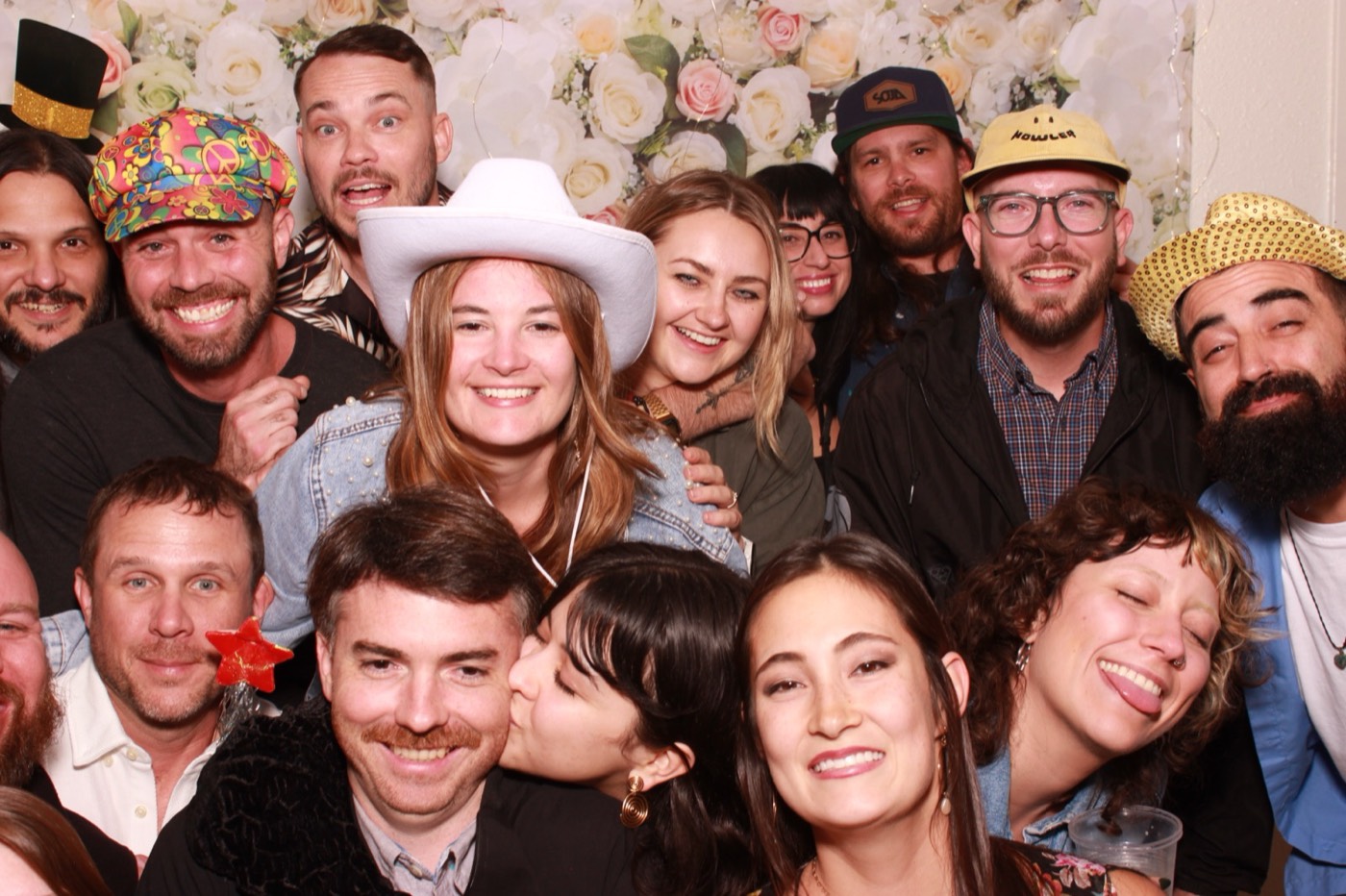 A crowd of guests in cowboy hats in front of a white flower wall at a wedding