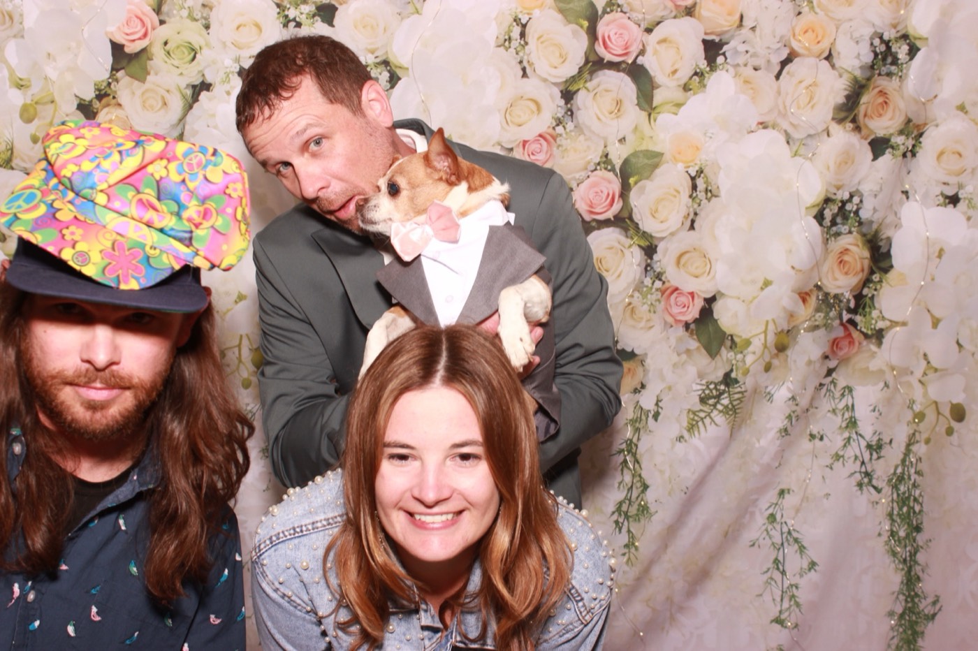 Guests in silly hats in front of a white flower wall at a wedding