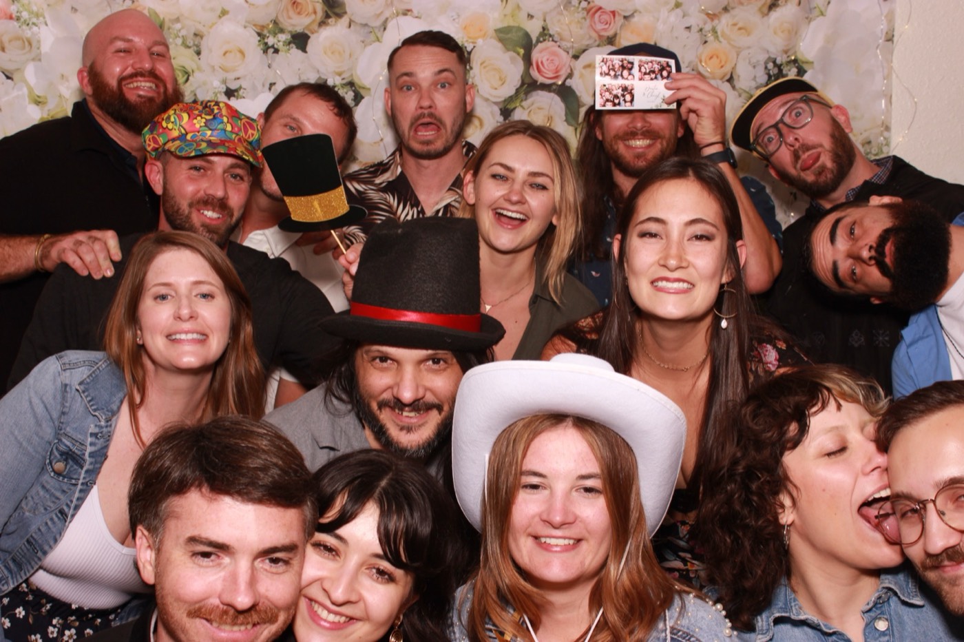 A big group of guests in cowboy hats in front of a white flower wall at a wedding