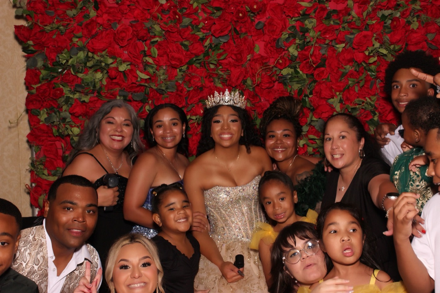 A quinceañera surrounded by family and friends in front of a red rose wall at a San Antonio quince party