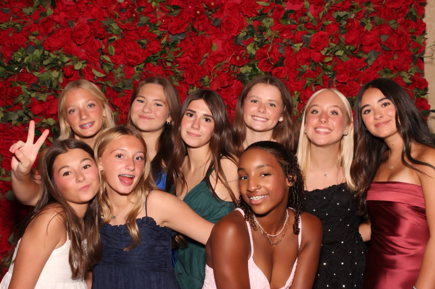 A big group of friends in party dresses in front of a red rose wall at a San Antonio quince party