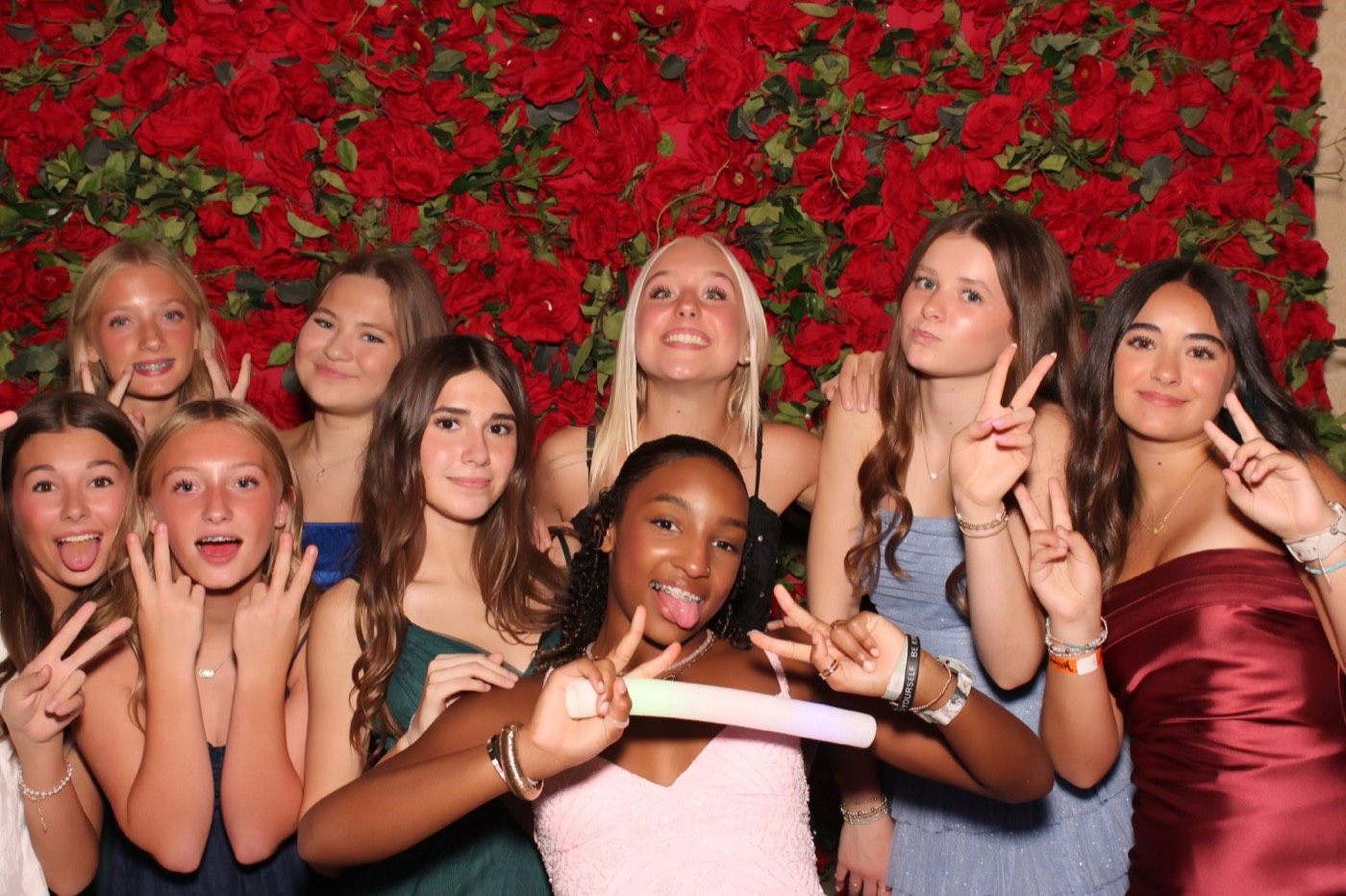 A group of friends holding up a sign in front of a red rose wall at a San Antonio quince party