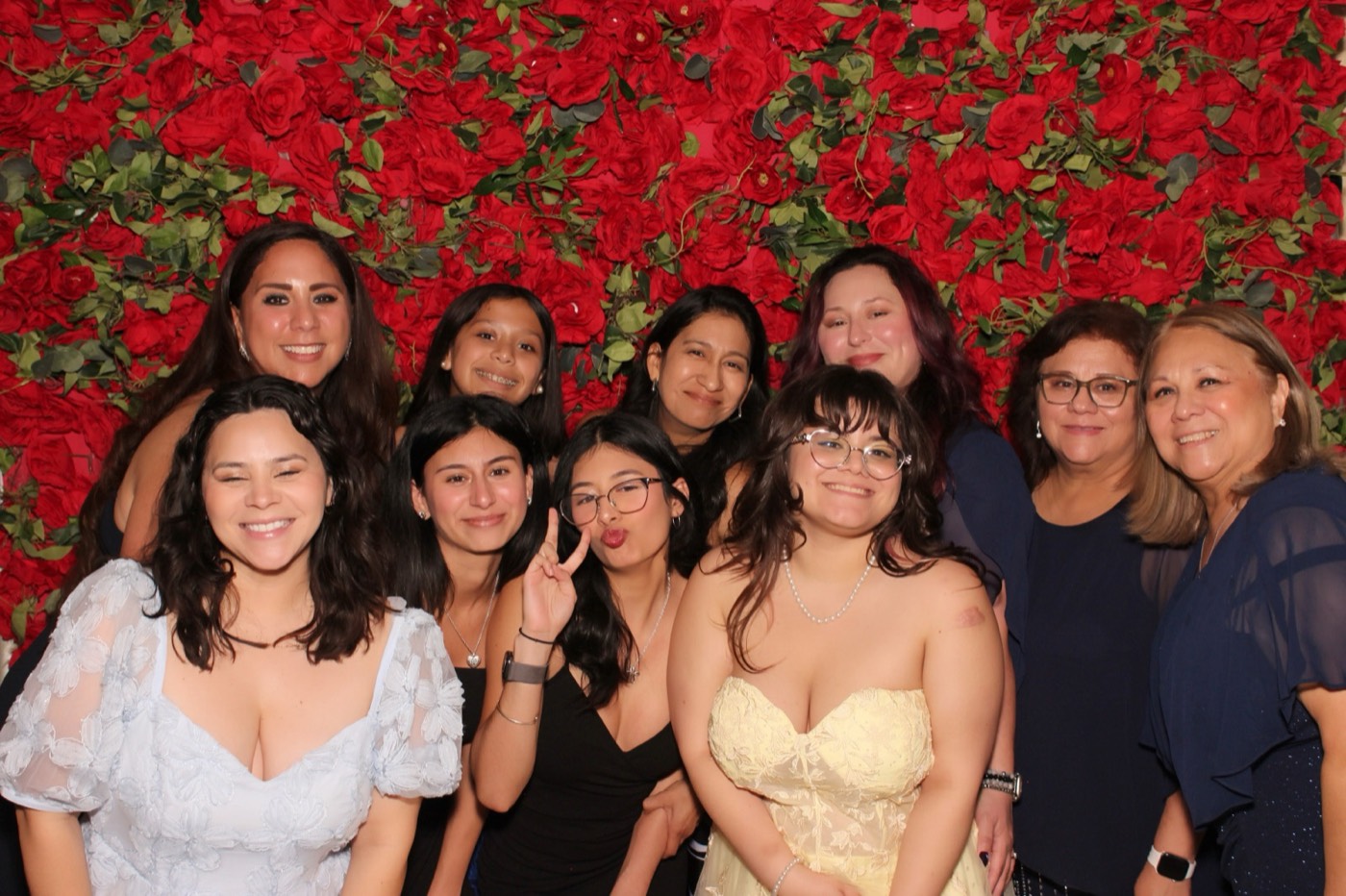 A big group of family and friends in front of a red rose wall at a San Antonio quince party