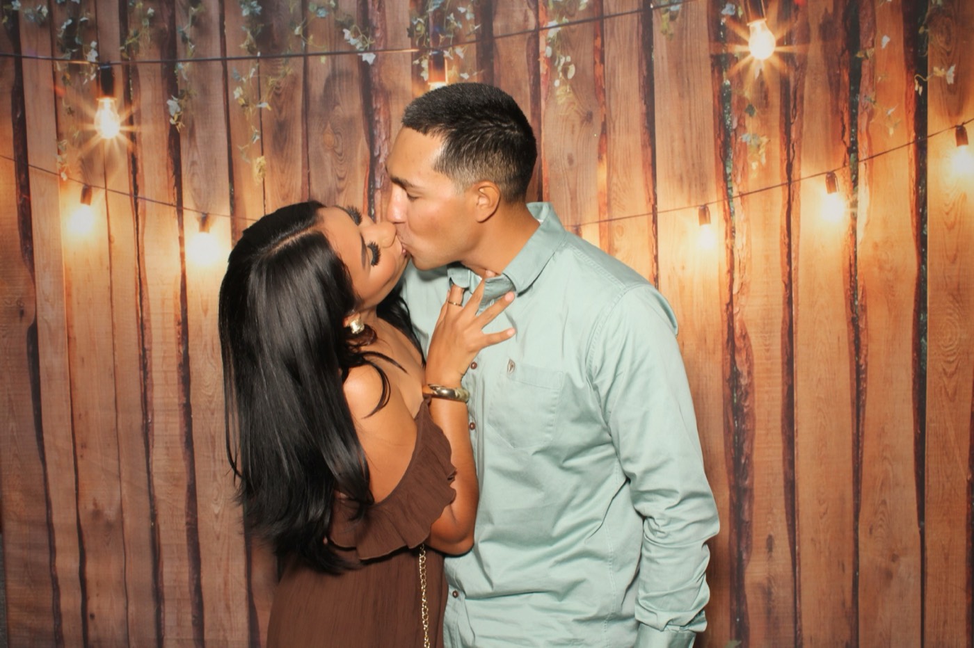 A couple sharing a kiss in front of a rustic wood wall with string lights at a wedding