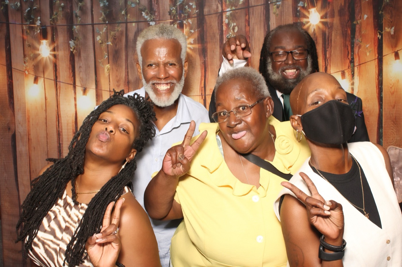 A family throwing peace signs in front of a rustic wood wall with string lights at a wedding