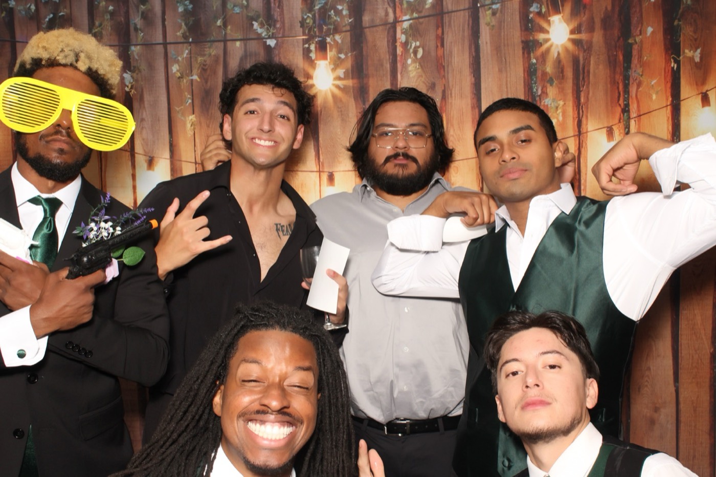 Groomsmen flexing together in front of a rustic wood wall with string lights at a wedding
